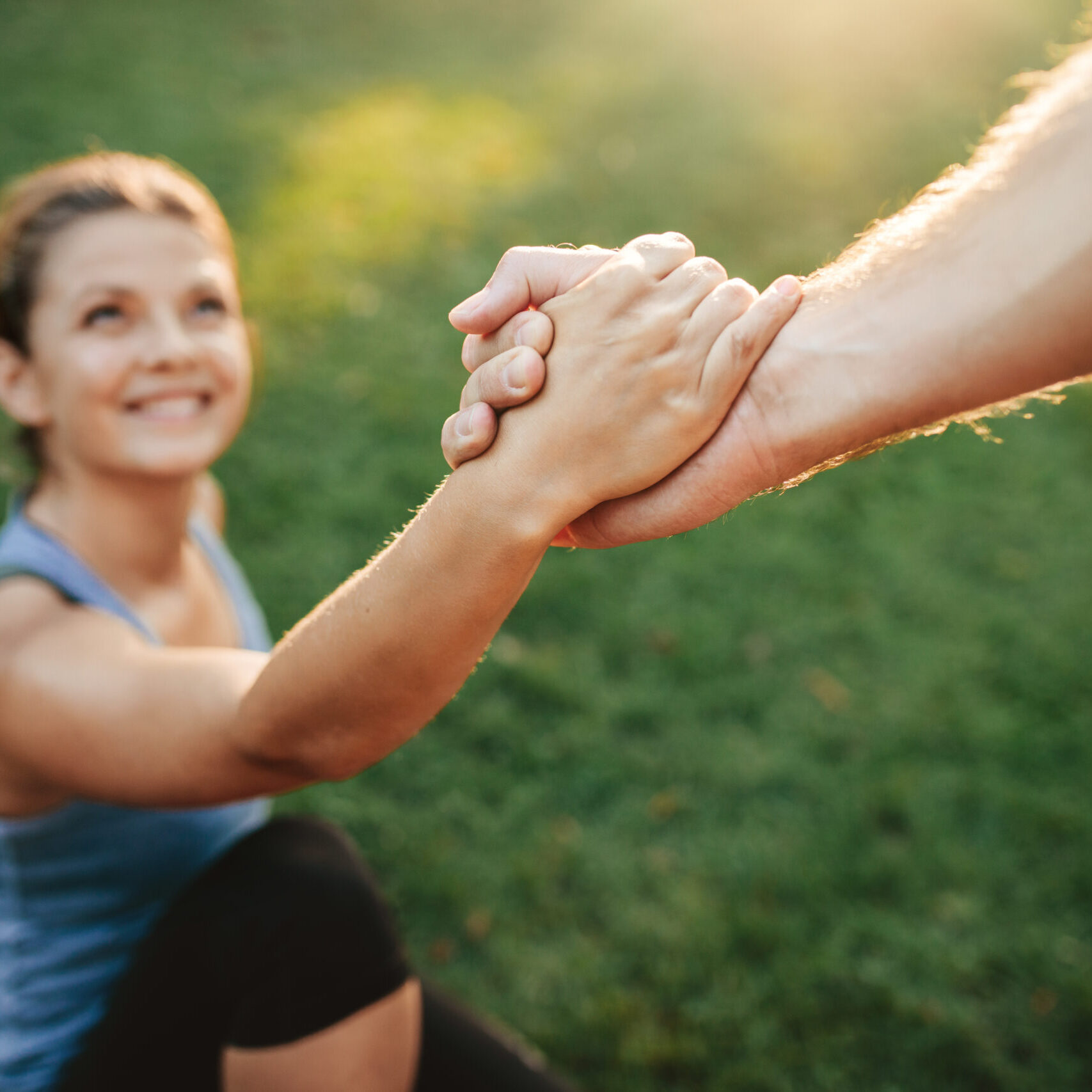 Close up shot of man helping woman to stand up. Focus on hands of couple exercising at park.